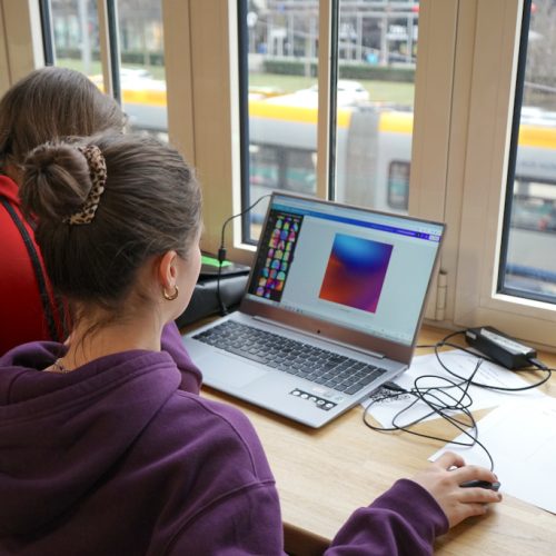 Zwei Personen in Rückenansicht sitzen an einem Laptop und bearbeiten ein Bild.