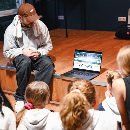 Teaserbild-start-Aktion-teasermood Ein Erwachsener sitzt neben einem Laptop, vor ihm befindet sich eine Gruppe junger Menschen, alle schauen gemeinsam auf den Bildschirm.